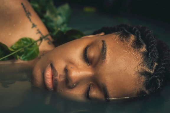 Sacred Rest & Radiance Beautiful woman with braids lying face-down with eyes closed, in a peaceful spa setting.